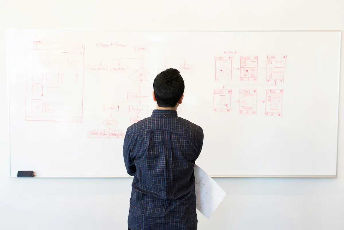 A man standing in front of a board looking at UI wireframes drawn on it