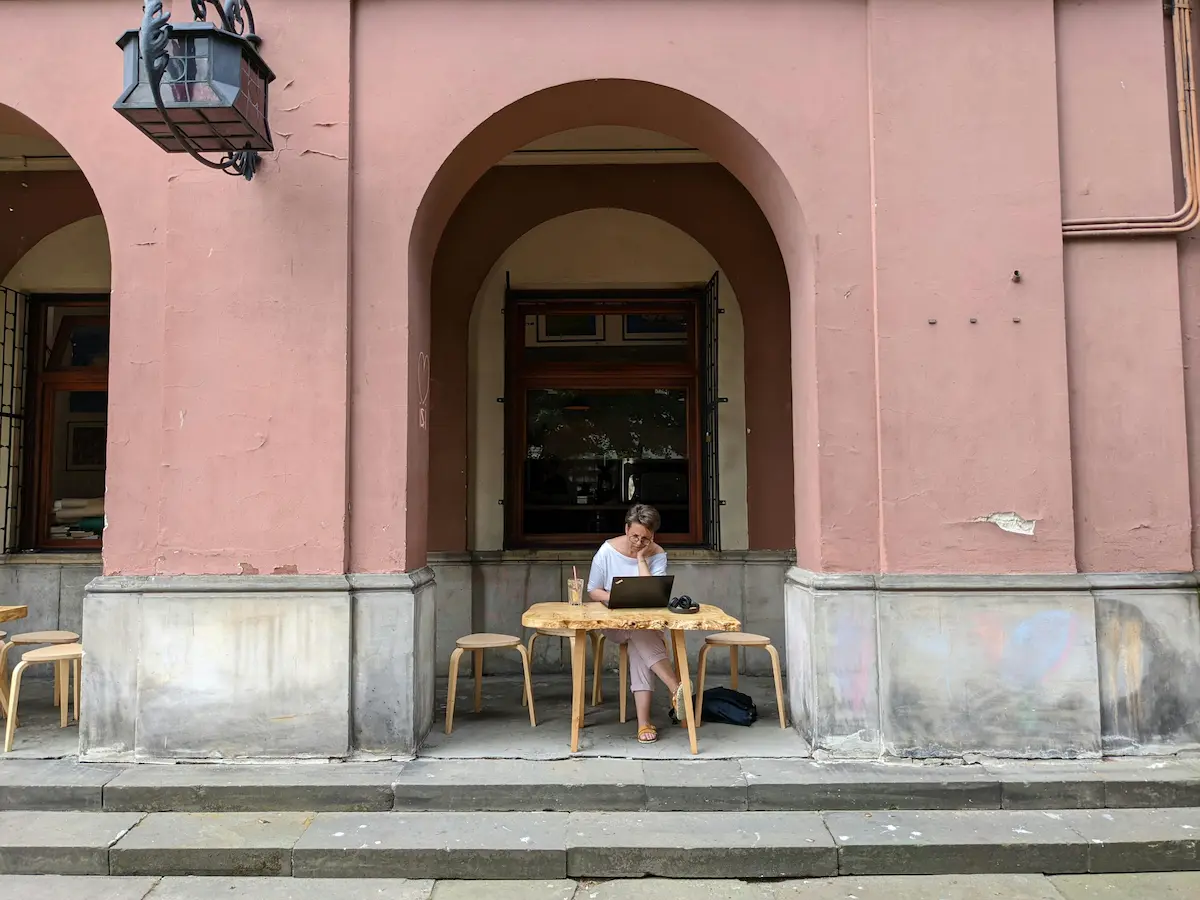 Kobieta siedząca przy stoliku na zewnątrz kawiarni, pracująca na laptopie